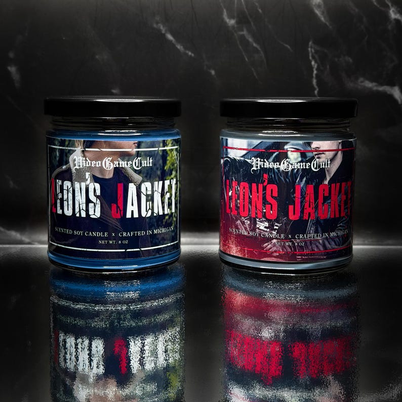 May include: Two glass jars with black lids. The labels read "Video Game Cult" and "Leon's Jacket" in white and red text. The jars are filled with blue wax and are 4 oz. each.