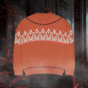 May include: A burnt orange crewneck sweater featuring a repeating dark navy cross pattern around the neckline and hem, with a wide band across the chest displaying a white geometric forest tree motif accented by small pink horizontal dashes.