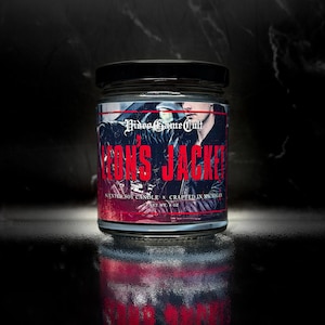 May include: A glass jar candle with a black lid. The label reads "Video Game Cult" and "Leon's Jacket" in red text. The candle has a black and white image of a person wearing a leather jacket. The candle is 8 oz.