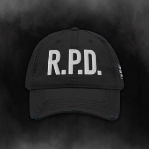 May include: Black baseball cap featuring the white letters "R.P.D." embroidered on the front. The cap has a distressed appearance with a curved peak. A classic style hat, suitable for casual wear.