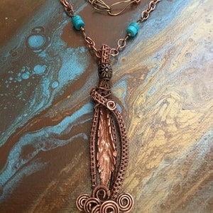 Peut inclure: Un collier avec un pendentif en fil de cuivre enroulé et une perle turquoise. Le pendentif présente un motif de feuille de cuivre avec un tourbillon de fil de cuivre en bas.