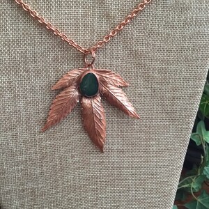 May include: A copper necklace with a green stone pendant shaped like a marijuana leaf.