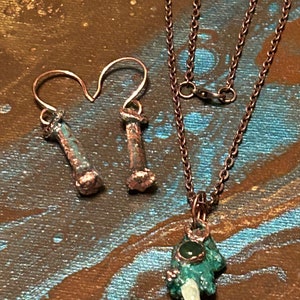 May include: A set of jewelry featuring a copper chain necklace with a green stone pendant and a pair of copper earrings with a green stone accent.