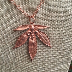 May include: A copper necklace with a pendant shaped like a stylized leaf with a fleur-de-lis in the center.