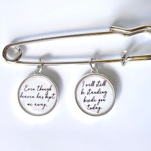 May include: Silver safety pin with two round charms. The charms have white backgrounds with black text. The left charm reads "Even though heaven has kept me away." The right charm reads "I will still be standing beside you today."