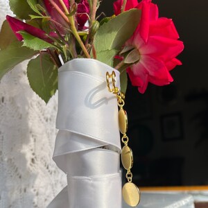 May include: A bouquet of red roses wrapped in white satin ribbon with a gold charm attached.