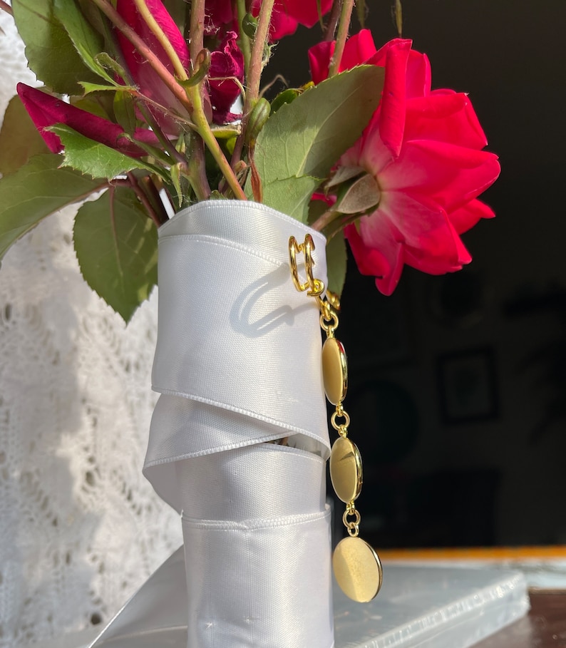 May include: A bouquet of red roses wrapped in white satin ribbon with a gold charm attached.
