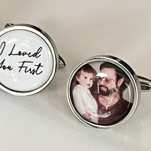 May include: A pair of silver cufflinks. One cufflink features a white background with the text "I Loved You First" in black script. The other cufflink features a photo of a man and a young child.