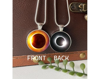 May include: A silver chain necklace with a round pendant featuring a solar eclipse image. The front of the pendant shows the sun with a dark ring around it, while the back shows the moon with a bright ring around it. The words "FRONT" and "BACK" are printed below the pendant.