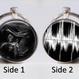 Puede incluir: Un llavero plateado con dos insertos de vidrio redondos. Un lado presenta una imagen de ultrasonido en blanco y negro de un bebé. El otro lado presenta una imagen de ultrasonido en blanco y negro del latido del corazón de un bebé.