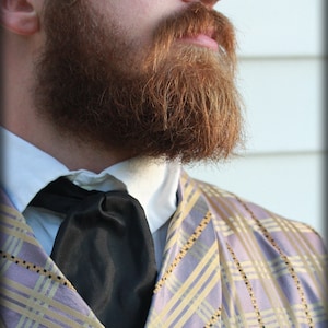 Puede incluir: Un hombre con una chaqueta de cuadros de color morado claro y dorado con una pajarita negra y una camisa blanca de cuello. Tiene una barba completa de color marr&oacute;n rojizo.