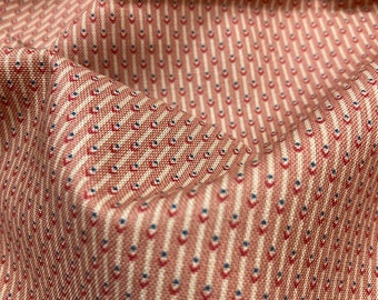 Op de afbeelding: Een geweven stof met een herhalend patroon van verticale crèmekleurige strepen, afgewisseld met kleine, afwisselend rode en blauwe geometrische ruitvormen. Het textiel heeft een getextureerd uiterlijk met plooien die diepte creëren.