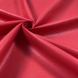 May include: Close-up of a smooth, red fabric with a subtle sheen. The fabric is folded and draped, showcasing its texture and drape.