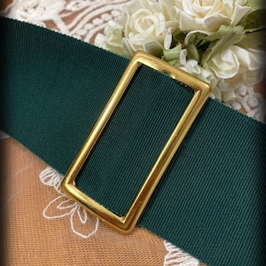 May include: A dark green fabric belt with a gold metal buckle. The buckle is rectangular with rounded corners.