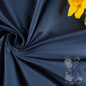 May include: A close-up of navy blue fabric with a subtle sheen, artfully draped and swirled. Two bright yellow daffodils are in the upper right corner. The fabric is likely used for apparel or home decor.