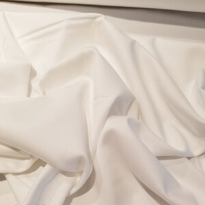 May include: White fabric with a smooth texture. The fabric is folded and draped, showing its soft and flowing nature.