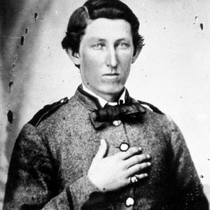 Puede incluir: Retrato en blanco y negro de un joven con uniforme militar y corbata de lazo. Lleva un anillo en la mano derecha y tiene la mano apoyada en el pecho.