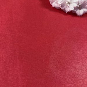 Puede incluir: Un fondo de tela roja s&oacute;lida con un grupo de flores de tela blanca en la esquina superior derecha. La tela tiene una textura sutil.