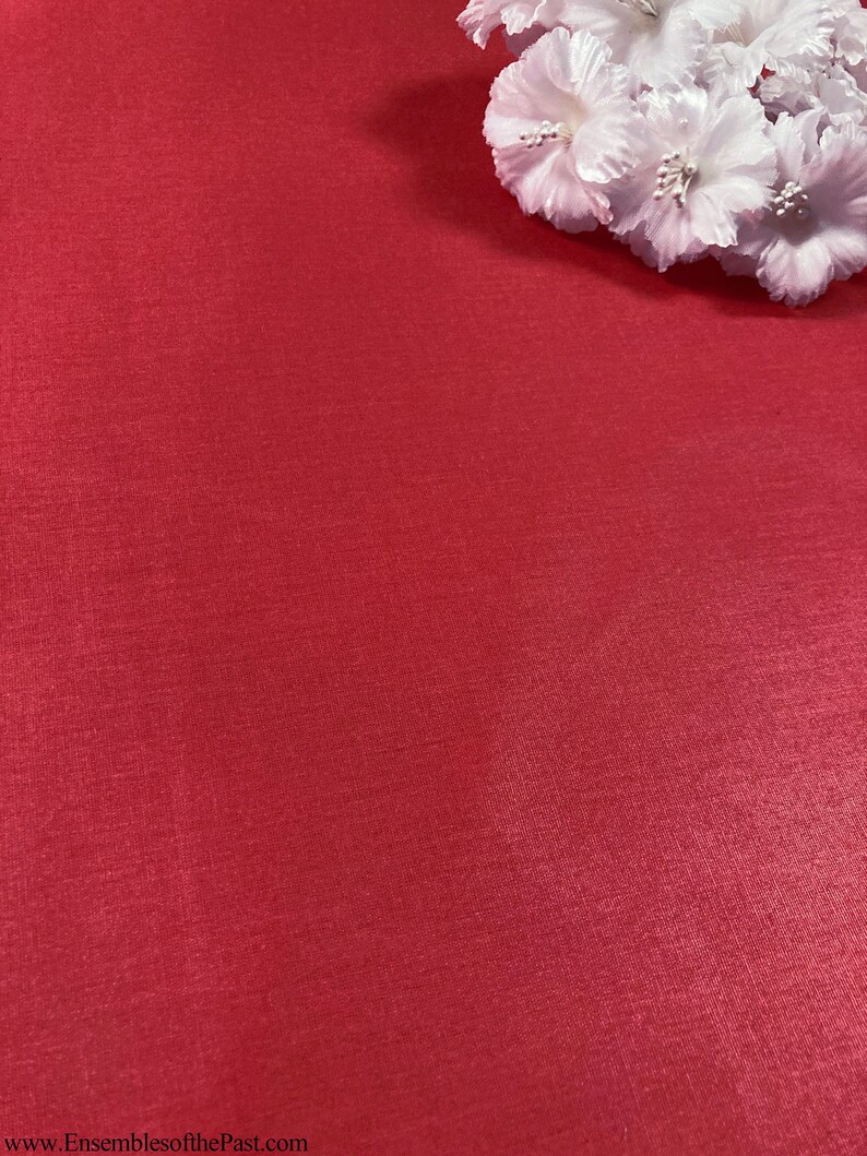 Puede incluir: Un fondo de tela roja s&oacute;lida con un grupo de flores de tela blanca en la esquina superior derecha. La tela tiene una textura sutil.