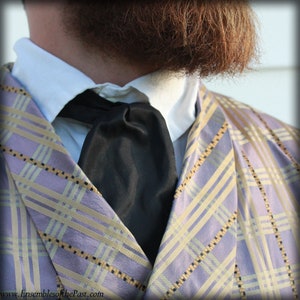 Puede incluir: Primer plano de la corbata y el cuello de un hombre. La corbata es negra y est&aacute; hecha de un tejido liso. El cuello es blanco y la camisa tiene un estampado de cuadros de color morado y amarillo claro.