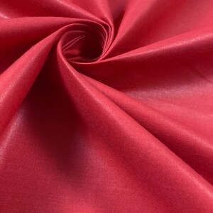 Puede incluir: Primer plano de una tela lisa de color rojo con un ligero brillo. La tela est&aacute; doblada en espiral, mostrando su textura y color.