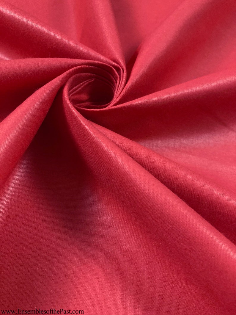 Puede incluir: Primer plano de una tela lisa de color rojo con un ligero brillo. La tela est&aacute; doblada en espiral, mostrando su textura y color.
