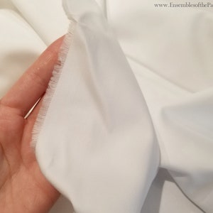 May include: Close-up of white cotton fabric with a raw edge. The fabric is smooth and has a slight sheen.