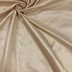 May include: A close-up of a smooth, beige fabric with a silky texture. The fabric is draped and folded, creating soft curves and folds.