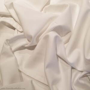 May include: White fabric with a smooth, silky texture. The fabric is draped and folded, creating soft, flowing lines.