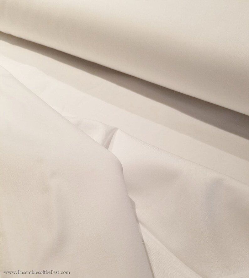 May include: White fabric, folded and rolled, showing the smooth texture and soft drape of the material.