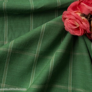 Könnte beinhalten: Grüner Stoff mit einem weißen und braunen Karomuster. Der Stoff ist gefaltet und ein Strauß rosa Rosen liegt auf dem Stoff.