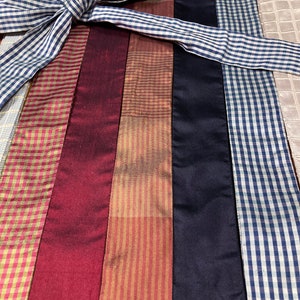 Puede incluir: Surtido de cintas de adorno en varios colores y patrones, incluyendo vichy, rayas y colores s&oacute;lidos. Las cintas est&aacute;n dispuestas en l&iacute;nea vertical y est&aacute;n atadas juntas con un lazo de cinta vichy azul y blanco. El texto "Ensembles of the Past" es visible en una etiqueta blanca.