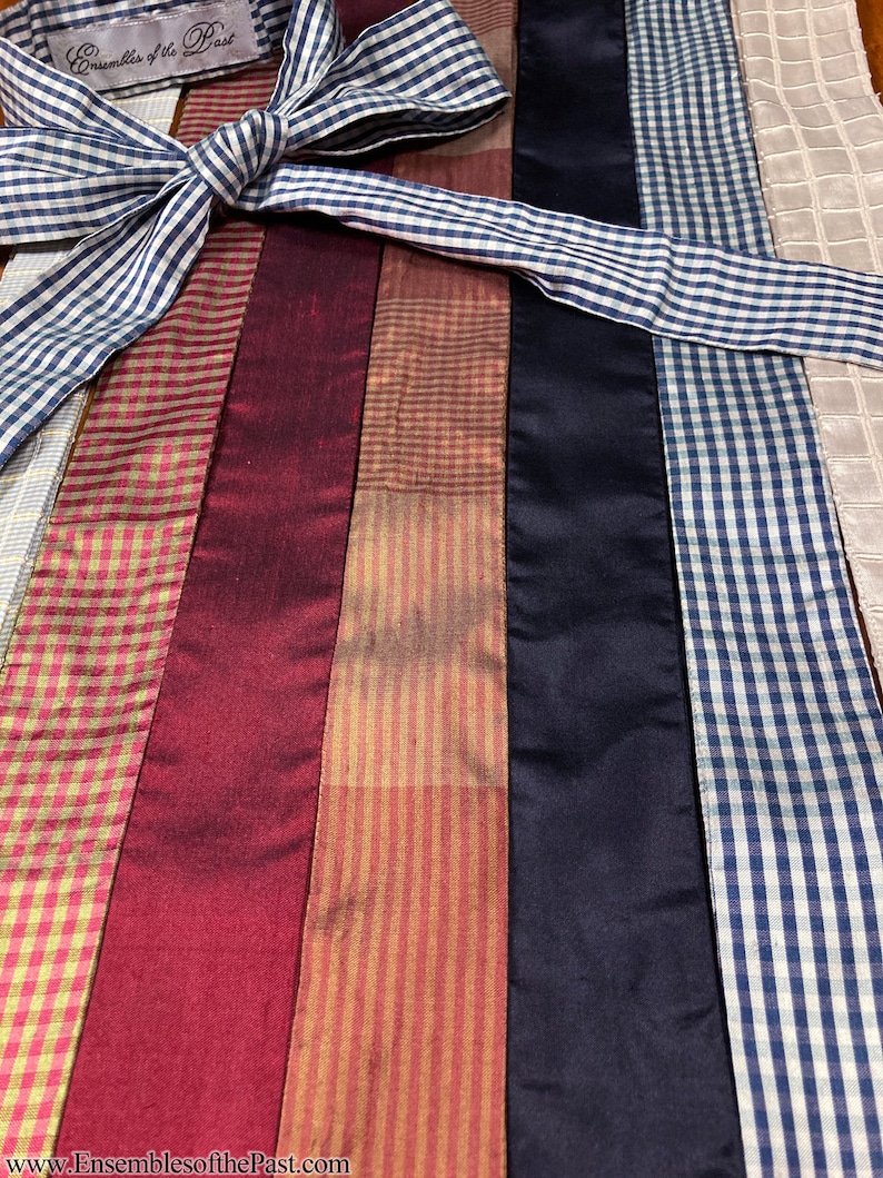 Puede incluir: Surtido de cintas de adorno en varios colores y patrones, incluyendo vichy, rayas y colores s&oacute;lidos. Las cintas est&aacute;n dispuestas en l&iacute;nea vertical y est&aacute;n atadas juntas con un lazo de cinta vichy azul y blanco. El texto "Ensembles of the Past" es visible en una etiqueta blanca.