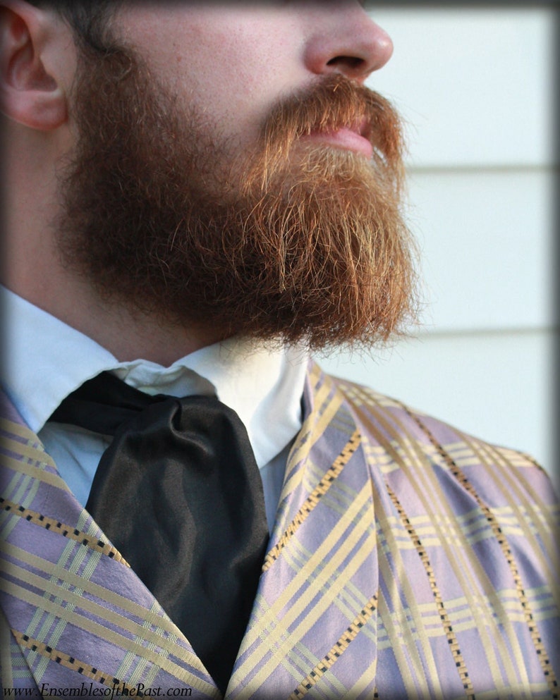 Puede incluir: Un hombre con una chaqueta de cuadros de color morado claro y dorado con una pajarita negra y una camisa blanca de cuello. Tiene una barba completa de color marr&oacute;n rojizo.