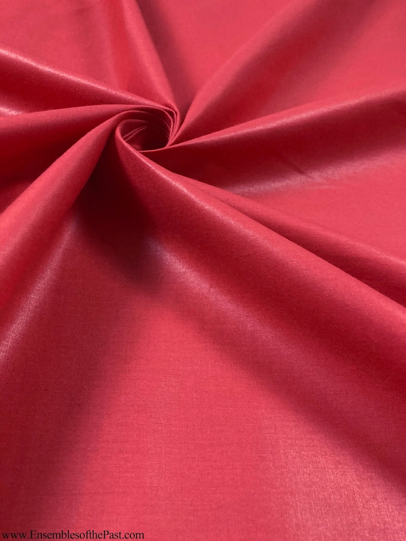 Puede incluir: Primer plano de una tela lisa de color rojo con un brillo sutil. La tela est&aacute; doblada y drapeada, mostrando su textura y ca&iacute;da.