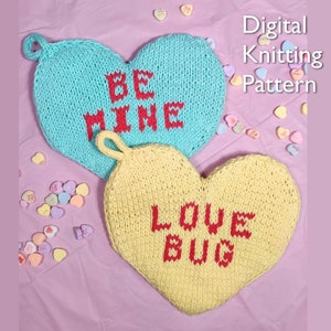 May include: Two knitted heart-shaped pot holders with a pink background. The blue pot holder says "BE MINE" in red yarn. The yellow pot holder says "LOVE BUG" in red yarn.