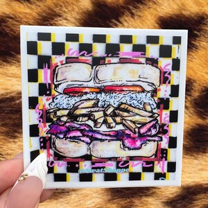 May include: A square sticker featuring a hand-drawn illustration of a sandwich with layers of meat, cheese, and vegetables. The sandwich is set against a black and yellow checkered background with pink scribbled accents and the text SwatShoppe.