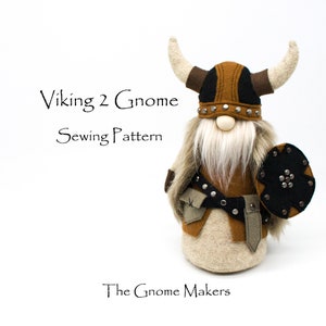 May include: A brown and black Viking gnome sewing pattern. The gnome is wearing a horned helmet with black and brown accents and a white beard. The gnome is holding a black shield with silver studs.