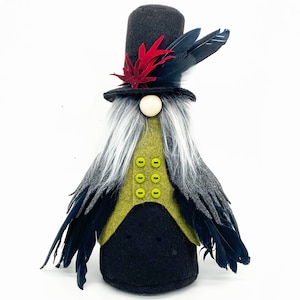 Peut inclure: Un gnome noir et vert portant un chapeau haut de forme avec des plumes rouges et une cape à plumes noires et grises. Le gnome a une barbe blanche et des boutons verts sur son gilet.