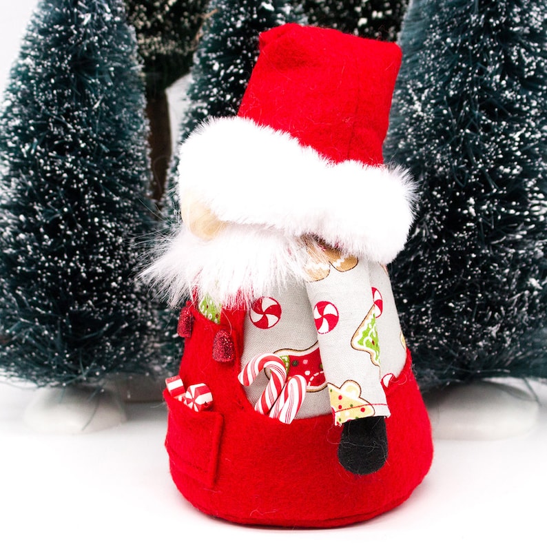 May include: A red and white Christmas gnome with a white fur trim hat and a candy cane pattern on the body. The gnome is holding candy canes in its hands.