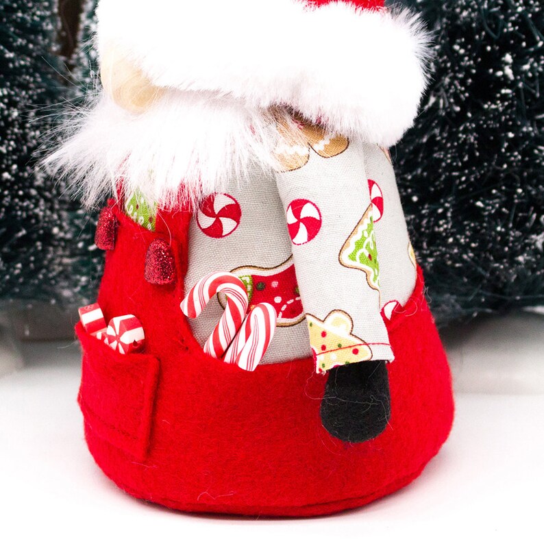 May include: A red and white Christmas gnome with a white fur hat and a white and gray patterned shirt. The gnome is holding candy canes in its pocket.