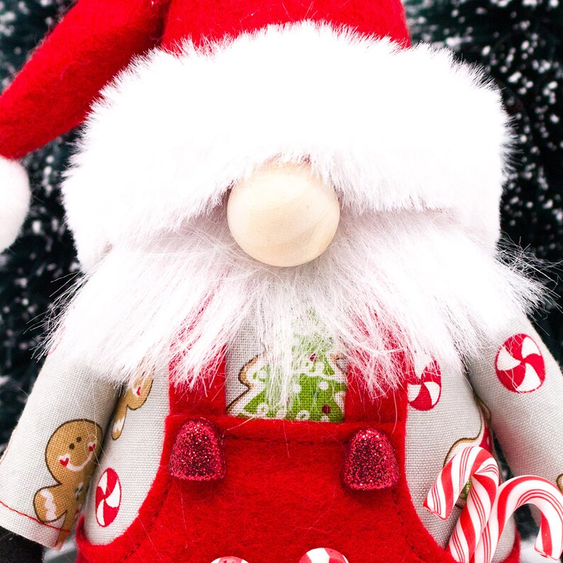 May include: A Christmas gnome with a white beard and red hat, wearing a red overall with a green Christmas tree design and candy cane accents.