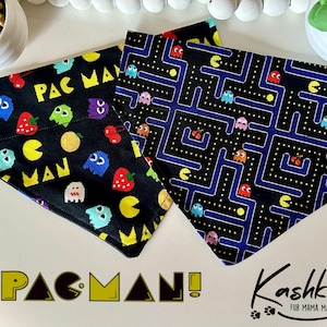 May include: Two black dog bandanas with a Pac-Man theme. One features Pac-Man characters and fruit, the other a maze design. The text "PAC MAN" and "Kashkas Fur Mama Made" are visible.