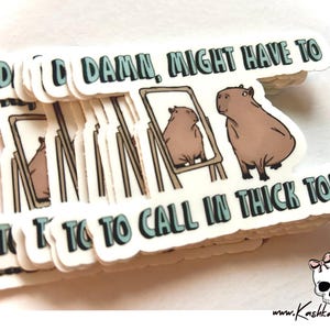 May include: A stack of white stickers with the text "DAD DAMN, MIGHT HAVE TO TO TO CALL IN THICK TODAY" in blue and green letters. The stickers feature a cartoon illustration of a capybara looking at itself in a mirror.