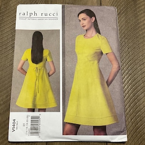 May include: A Ralph Rucci sewing pattern from Vogue Patterns. The pattern shows a yellow dress with short sleeves and a fitted waist. The dress has a round neckline and a flared skirt. The pattern number is V1404, and the size range is 14-22.