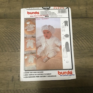 May include: Burda sewing pattern 9944 for a baby christening outfit. The pattern includes a bonnet, a long gown, a short romper, and a jacket. The pattern is printed on white paper with black and red text. The pattern is for sizes 50 to 80 cm.