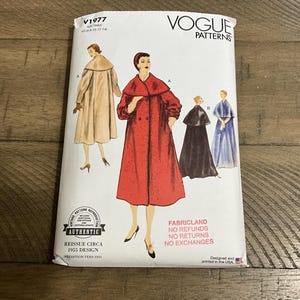 May include: A Vogue Patterns V1977 sewing pattern envelope for a 1955 design. The white paper envelope features illustrations of a long coat with a cape collar in red, beige, black, and blue, along with text including V1977, Vogue Patterns, and Fabricland.