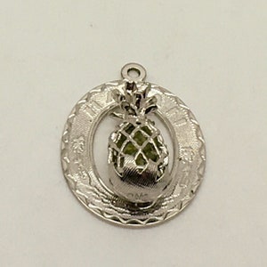 May include: Silver charm with a green pineapple design in the center and the words "Aloha" and "Hawaii" around the edge.