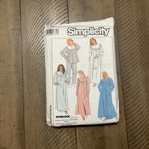 May include: A Simplicity sewing pattern packet showing illustrations of women's sleepwear designs. The packet includes images of a pajama set, nightgowns, and a robe. The packet is white with the Simplicity logo and product details.