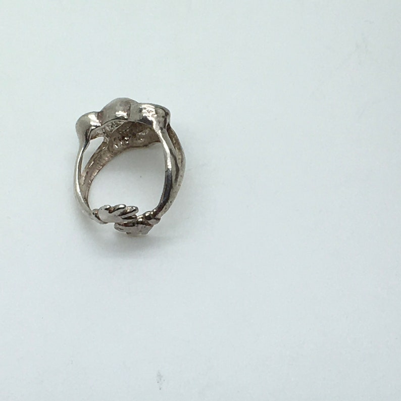 May include: Silver ring with a unique design featuring two hands clasped together. The ring is made of sterling silver and has a polished finish.